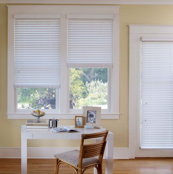 White pleated blinds in a room with a desk, chair, and window. Sunlight streams through the blinds.