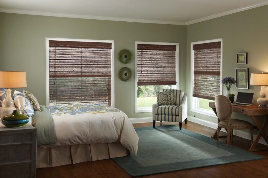 Bedroom with woven shades, sage walls, a bed, chair, desk, and area rug.
