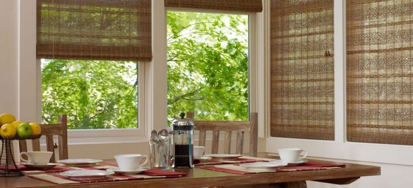 Breakfast table by a window with woven shades, overlooking green trees.