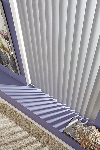 White pleated window blinds casting shadows on a light purple windowsill.