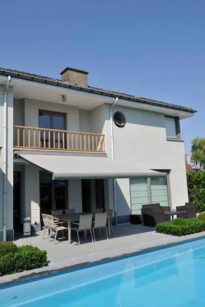 Two-story white house with a patio, awning, and swimming pool on a sunny day.