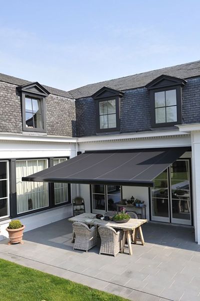 Patio with retractable black awning, table, chairs, and house with slate roof.
