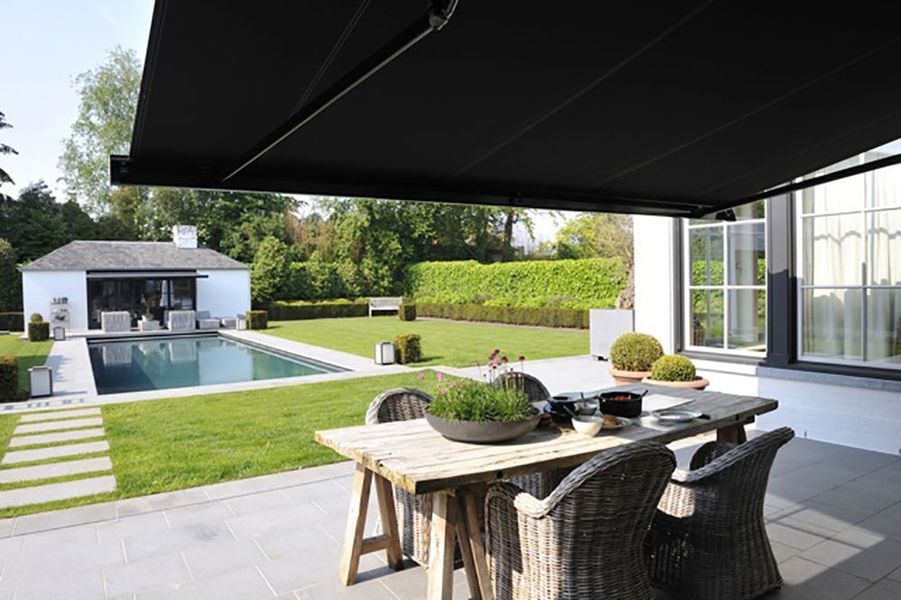 Patio with retractable black awning, table and chairs, pool, and white building.