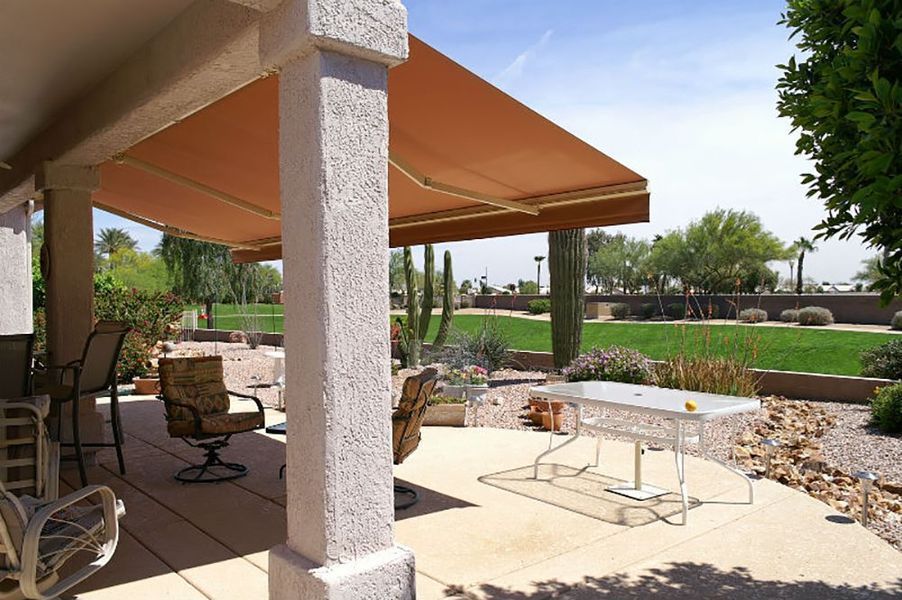 Patio with tan awning, concrete pillars, table, chairs, and desert landscape in background.