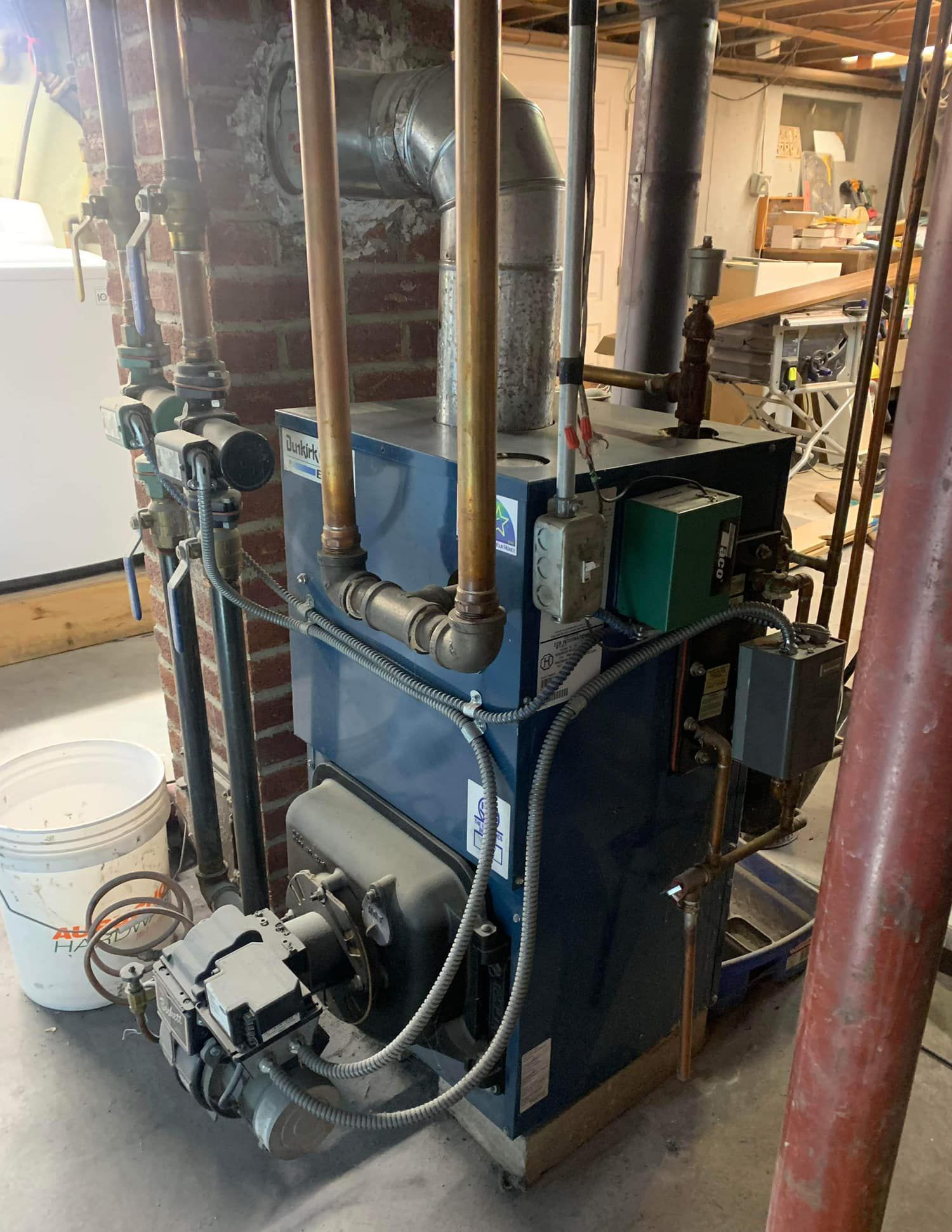 A blue boiler is sitting in a basement next to a brick wall.