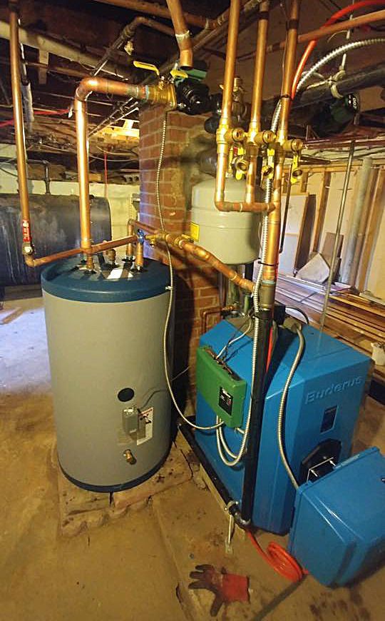 A blue water heater is sitting next to a gray water heater in a basement.