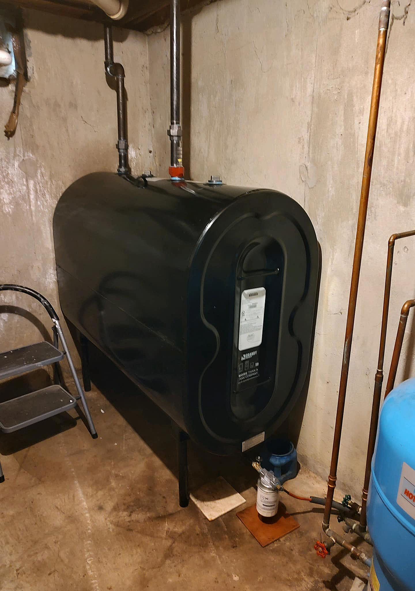 A large black tank is sitting in a basement next to a ladder.