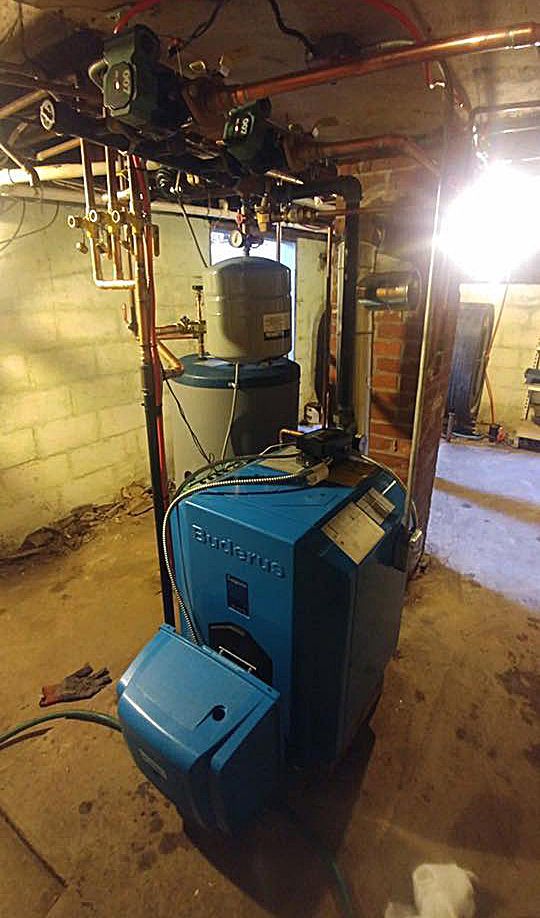 A blue boiler is sitting in a basement next to a water heater.