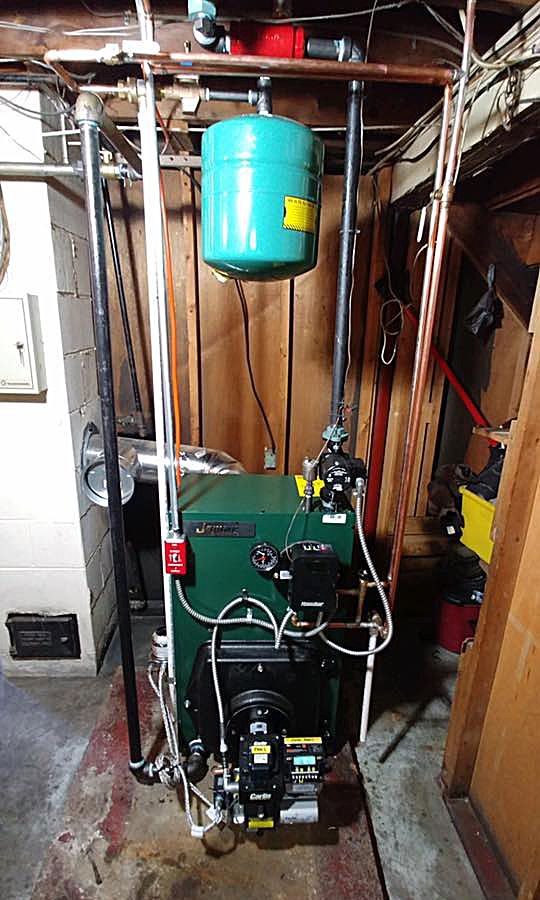 A green boiler is sitting in a basement next to a green tank.