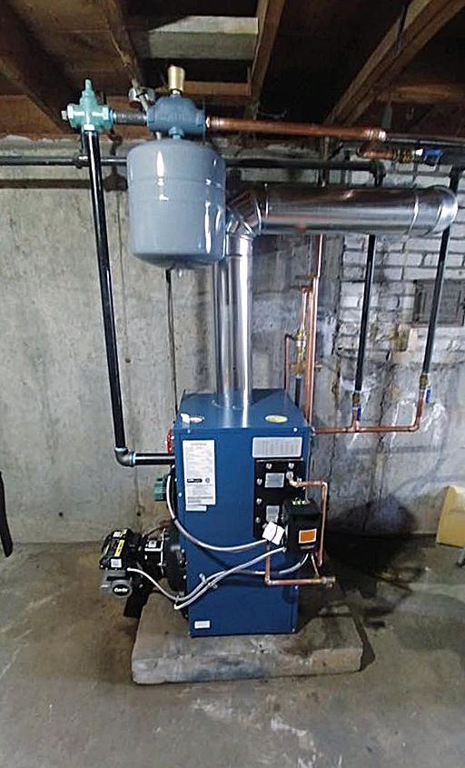 A blue boiler is sitting in a basement next to a brick wall.