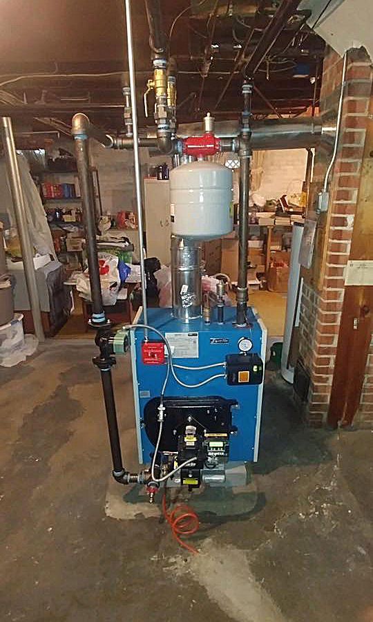 A blue boiler is sitting in a basement next to a brick wall.