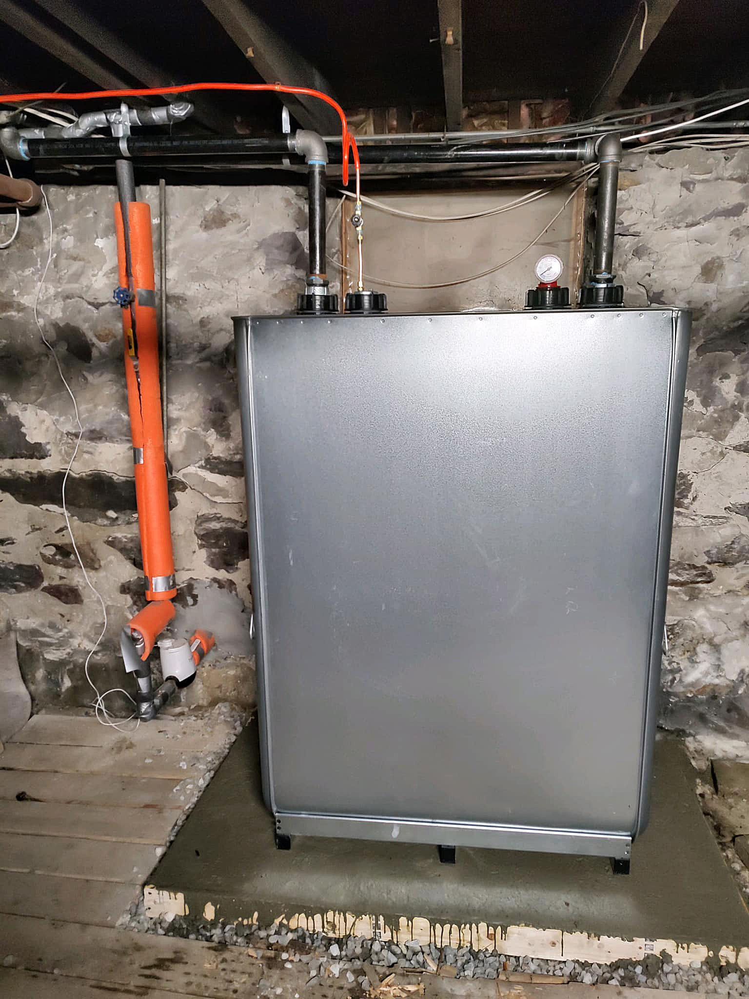 A large metal tank is sitting in a basement next to a stone wall.