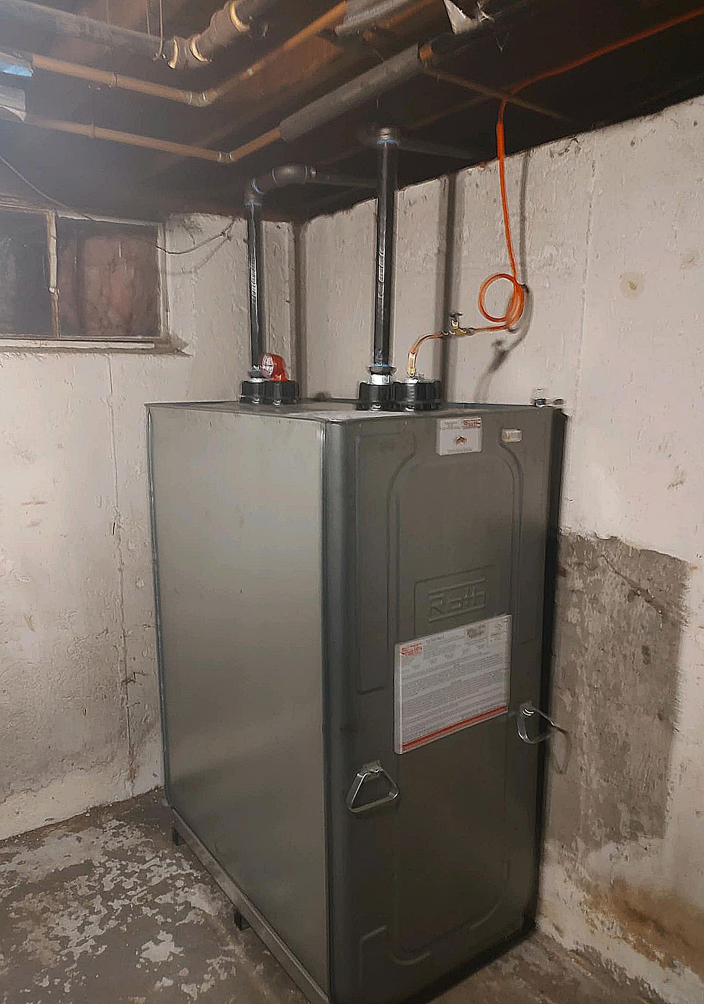 A water heater is sitting in a basement next to a wall.