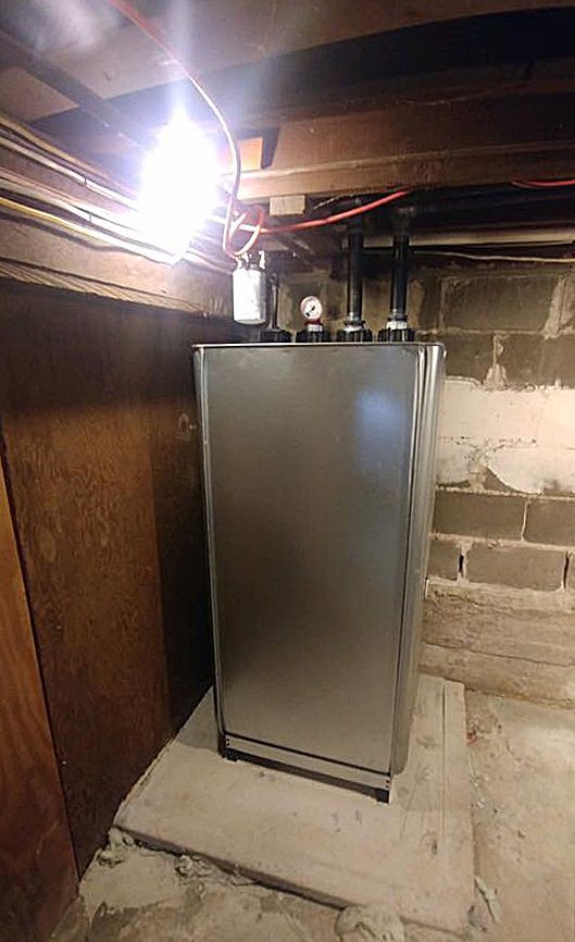 A stainless steel water heater is sitting in a basement next to a brick wall.