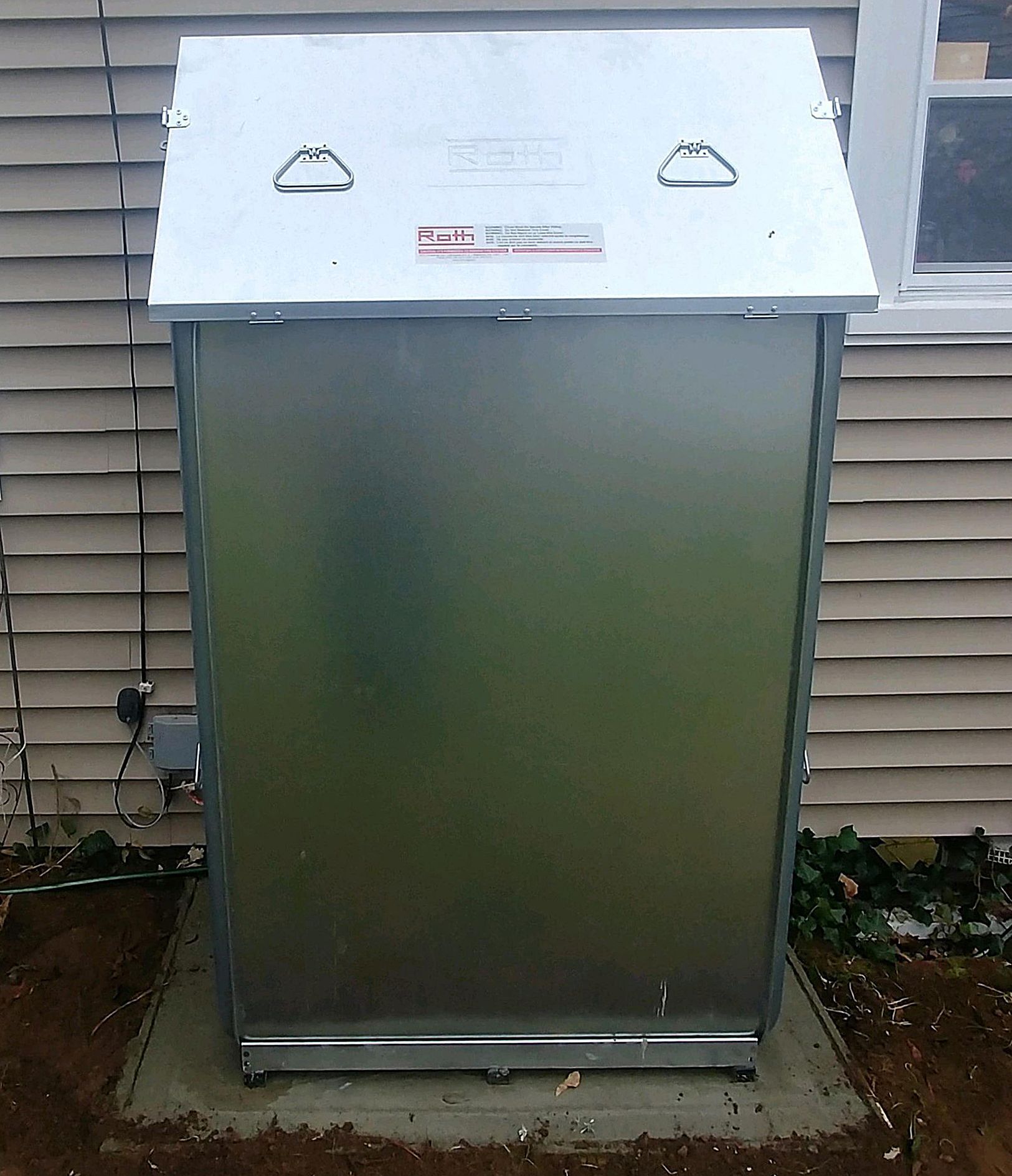 A stainless steel trash can is sitting outside of a house