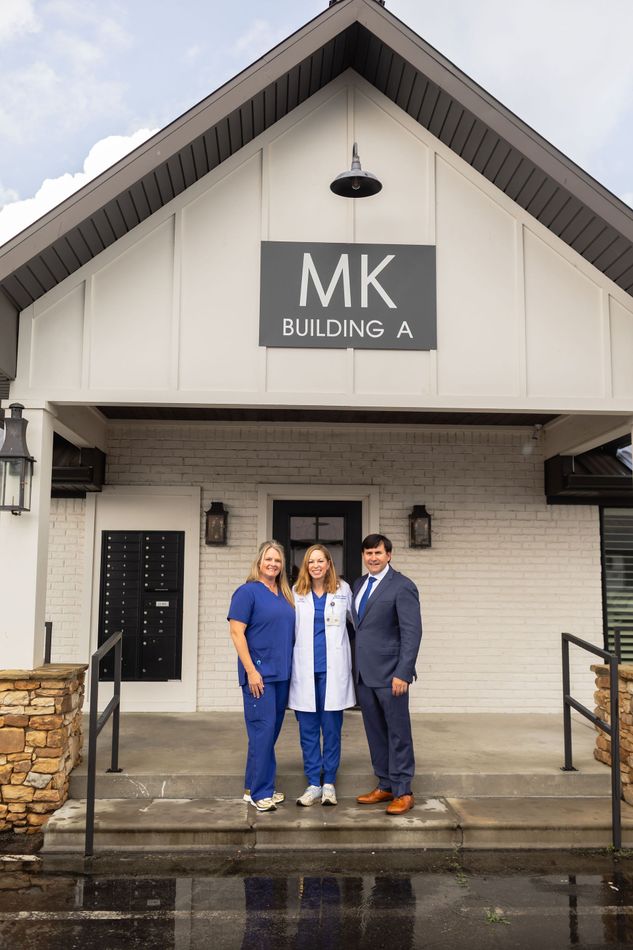 Three people stand outside MK Building A, a white building with a peaked roof and wet steps.