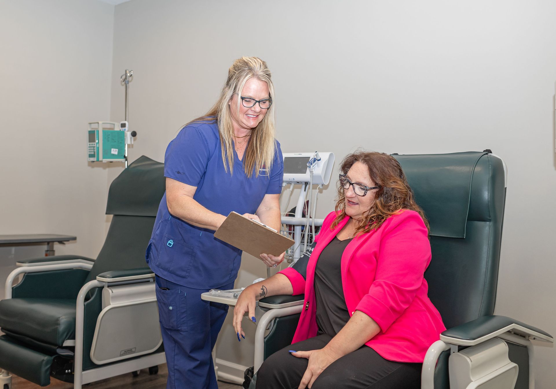 Nurse taking blood pressure from seated patient in a clinic exam room.