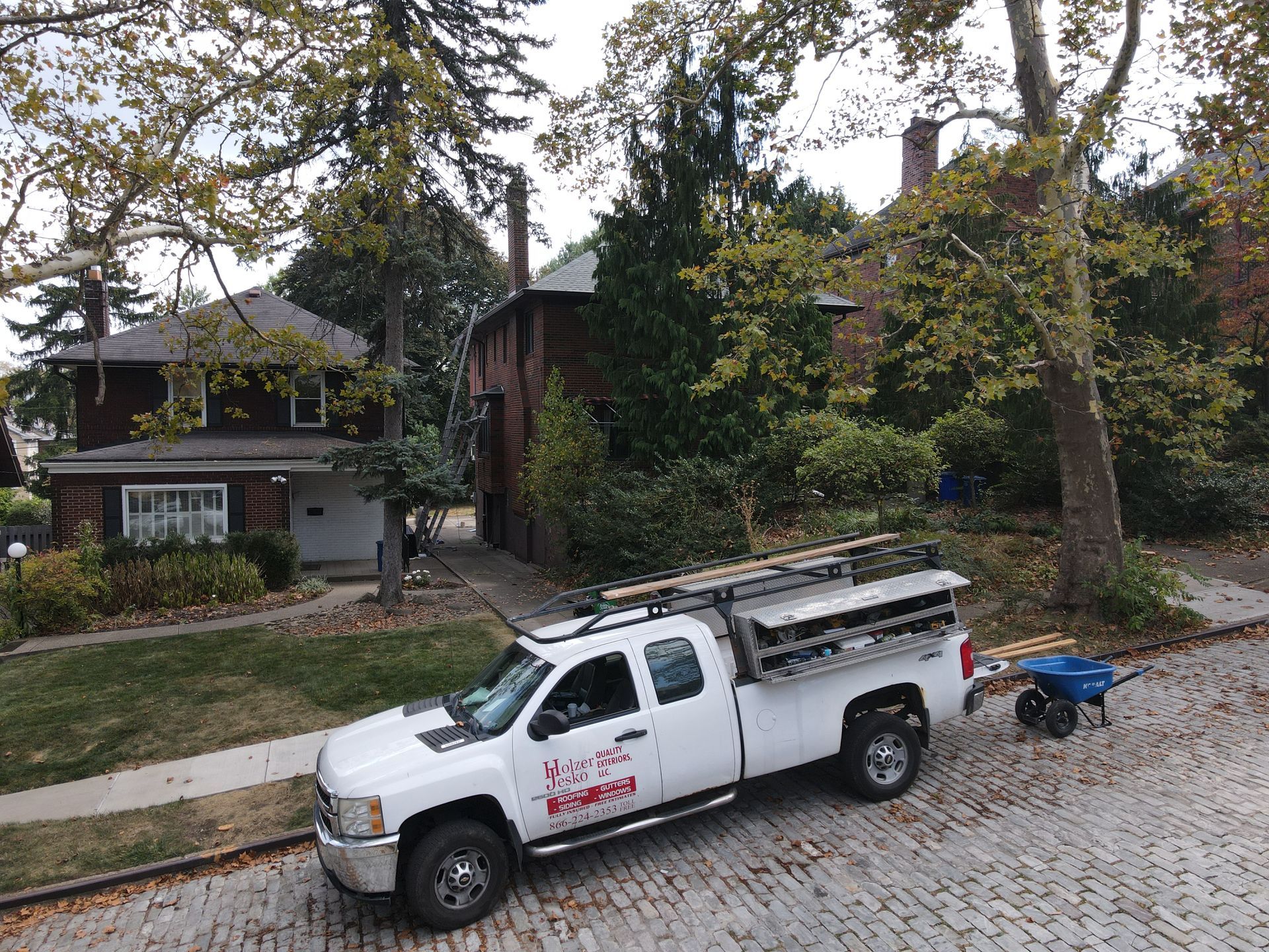 White pickup truck parked on a cobblestone street in front of houses. Tree branches arch over the truck.