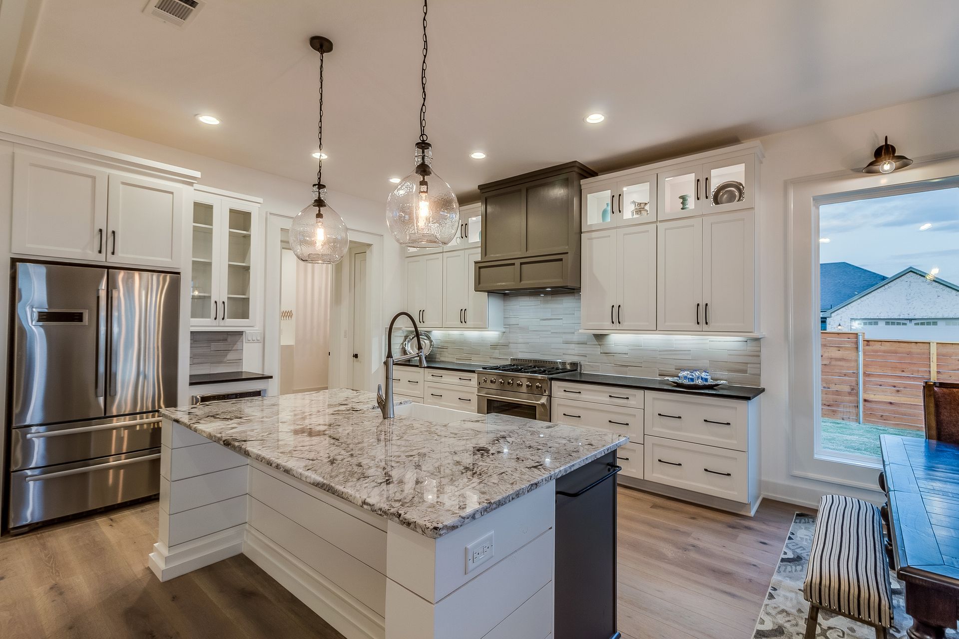 Bright modern kitchen with white cabinets, granite island, stainless steel appliances, and pendant lights.