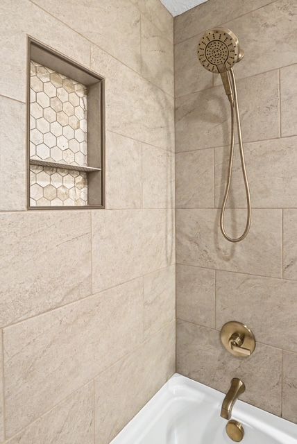 Shower corner with beige tile, brass showerhead, and small window with hexagonal glass.