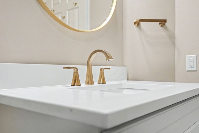Modern bathroom vanity with white sink, gold faucet, and round mirror