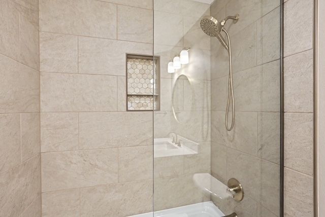 Tiled shower with glass door, wall niche, and chrome showerhead in a beige bathroom.