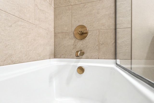 White bathtub corner with beige tile wall and brass shower fixtures