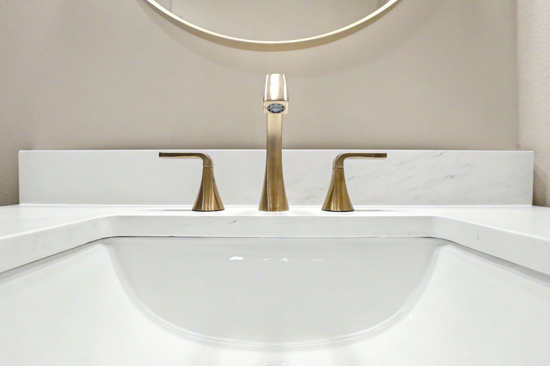 Modern white bathroom sink with brass faucet and round mirror above the vanity