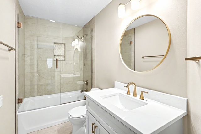 Bright bathroom with tub-shower, white vanity, and round gold-framed mirror