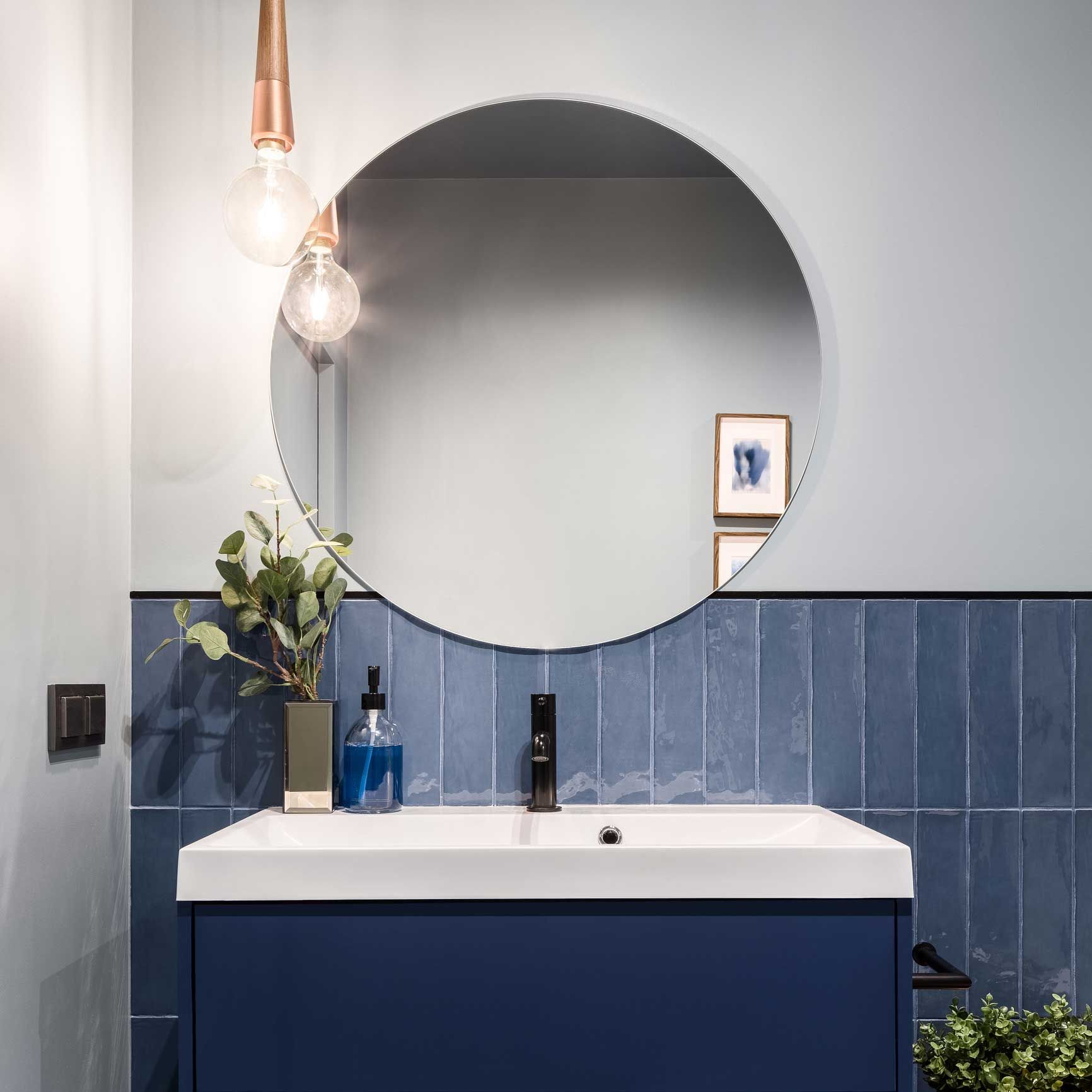 Modern bathroom vanity with round mirror, blue cabinets, white sink, and hanging pendant light