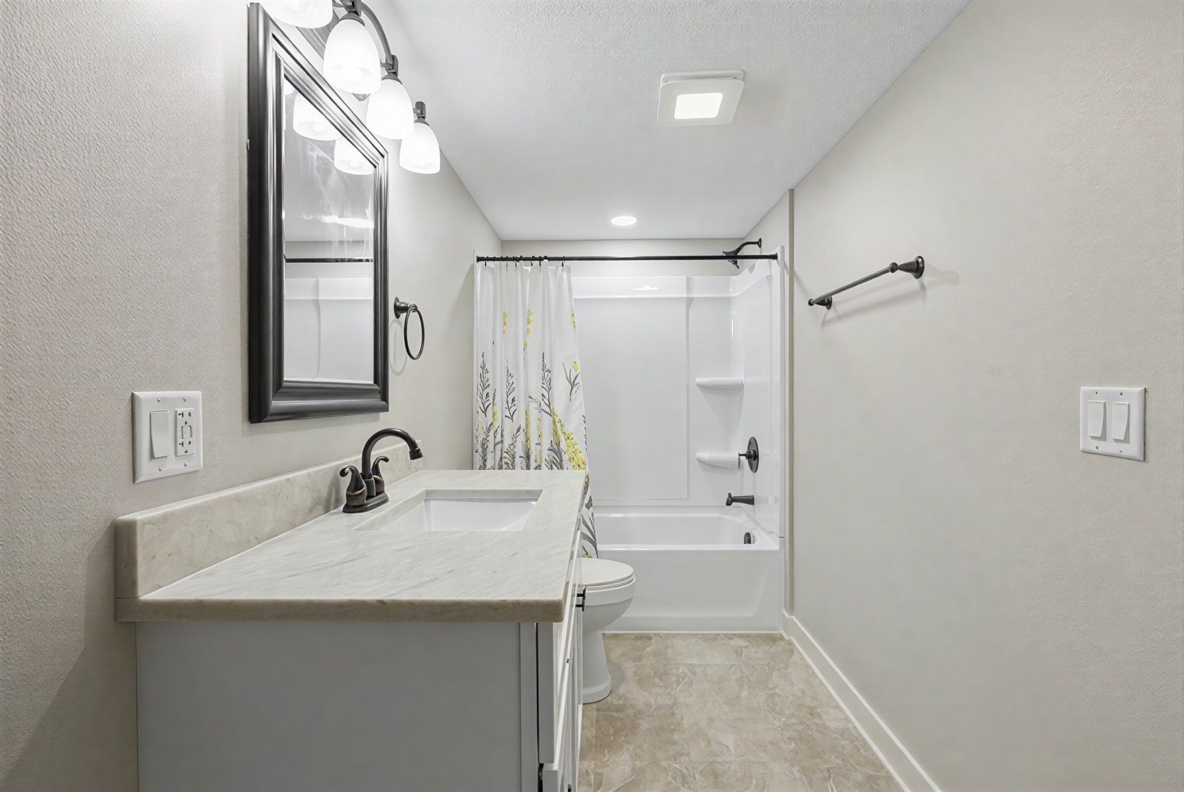 Bright bathroom with vanity, mirror, toilet, and tub with shower curtain along a narrow hallway.