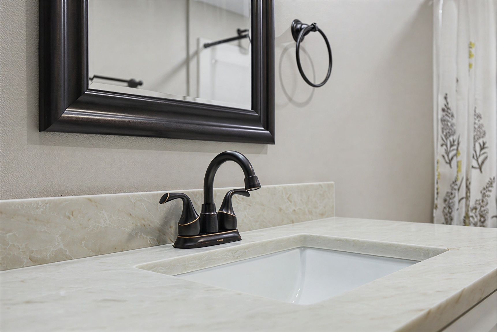 Bathroom sink with black faucet, wall mirror, and light stone countertop.