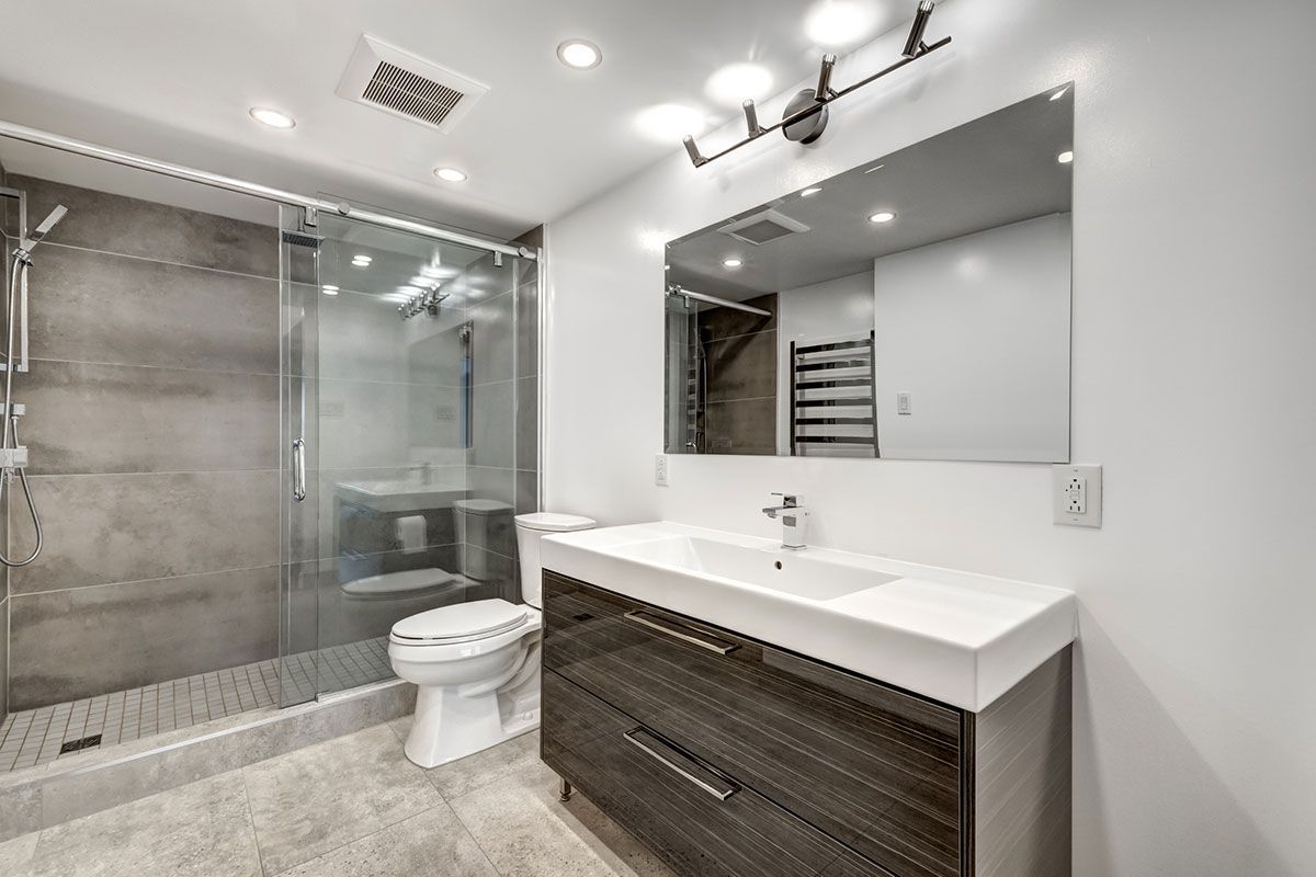 Modern bathroom with glass shower, toilet, and dark vanity with large mirror.