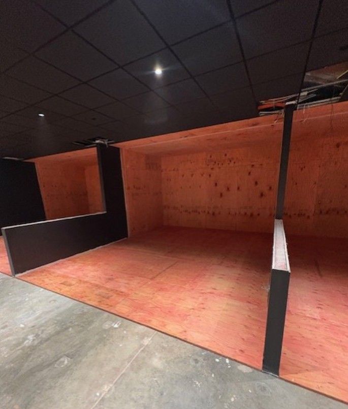 Empty indoor booth with orange floor, black walls, and a dark ceiling under construction or setup
