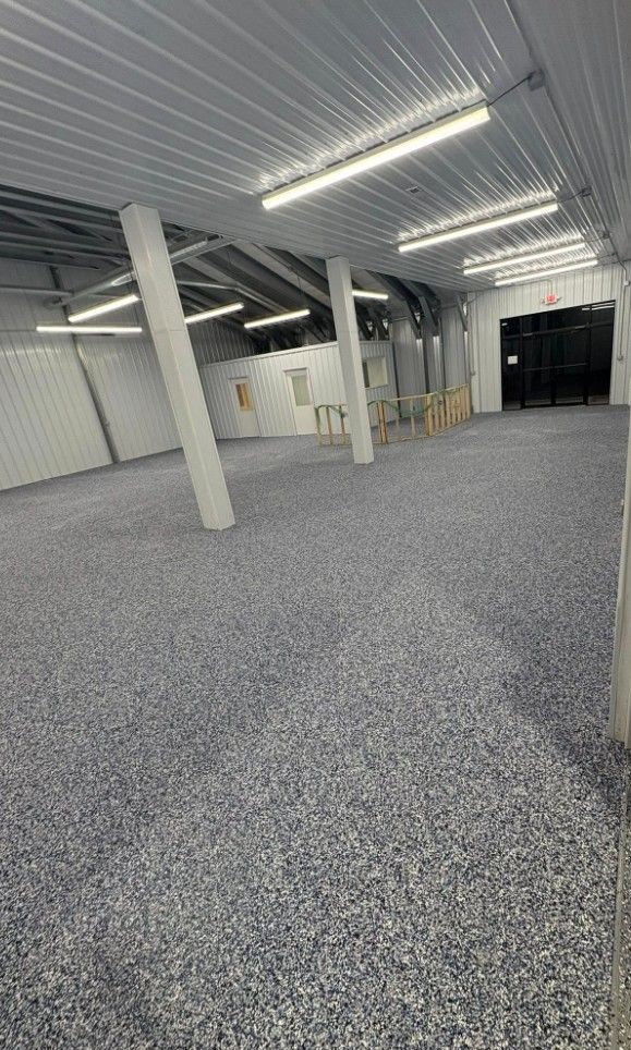 Empty industrial warehouse with gray carpeted floor, white ceiling lights, and support columns