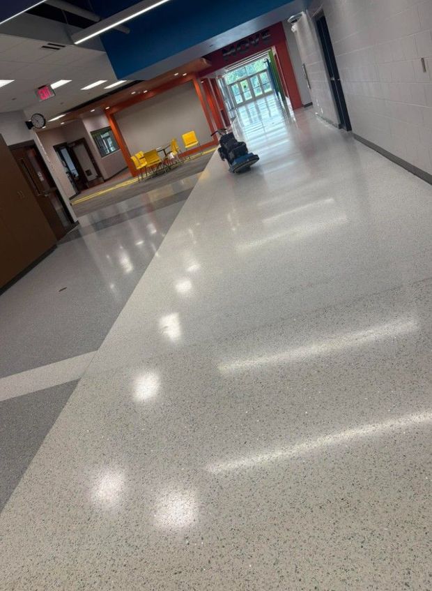 Bright school hallway with glossy floor, lockers, and doors leading to a glass exit.