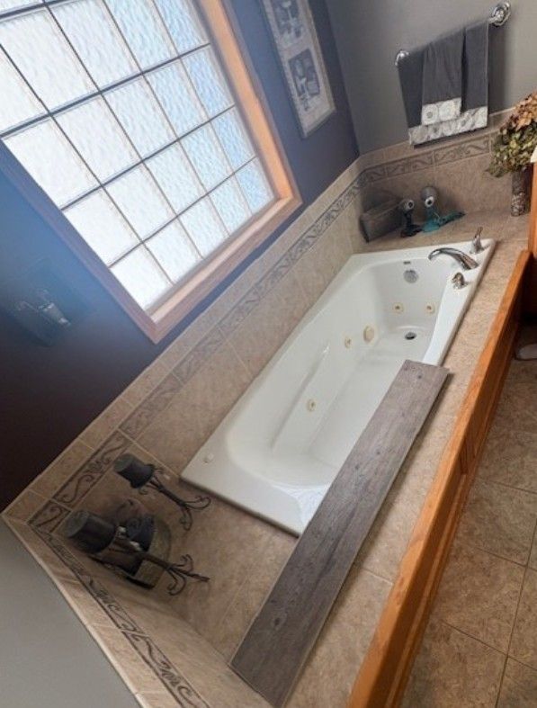 Bathroom with a white soaking tub beside a window and tiled floor.