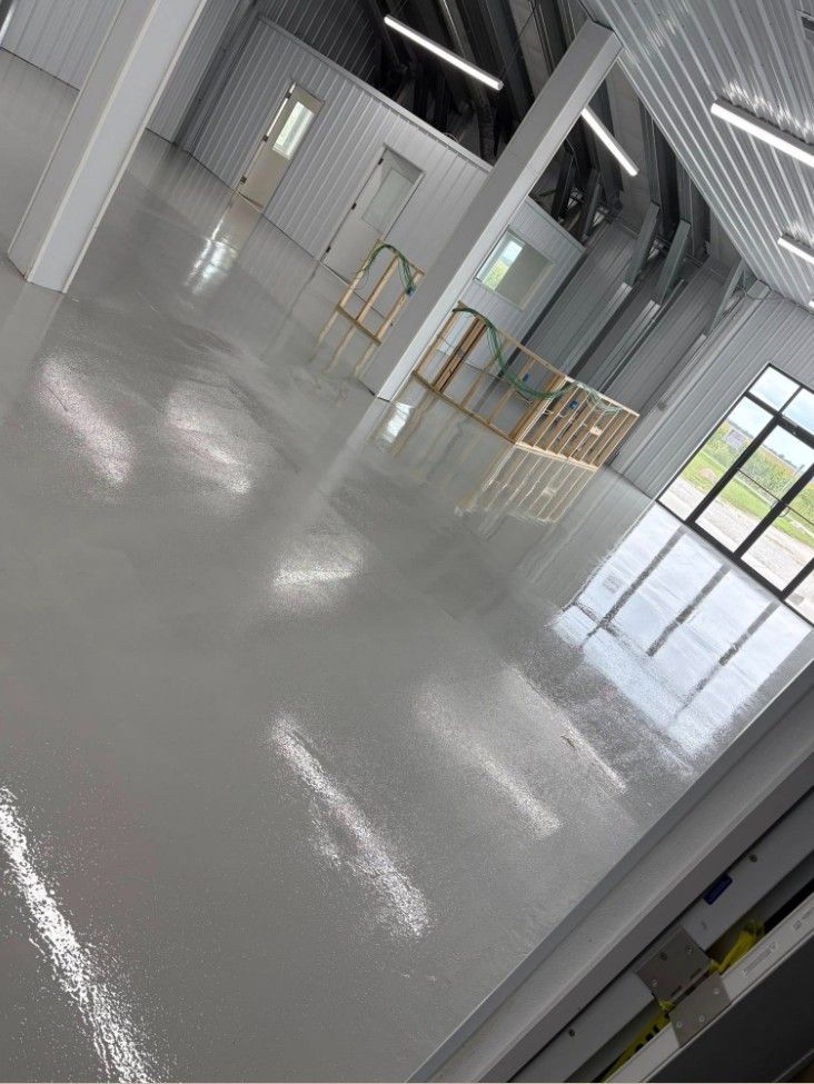 Empty industrial hallway with glossy gray floor, metal railings, and bright windows.