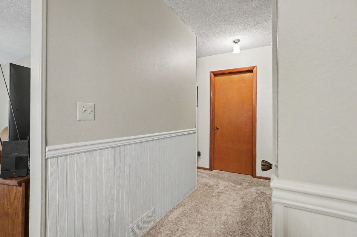 Hallway with beige carpet, white wainscoting, and a wooden door at the end.