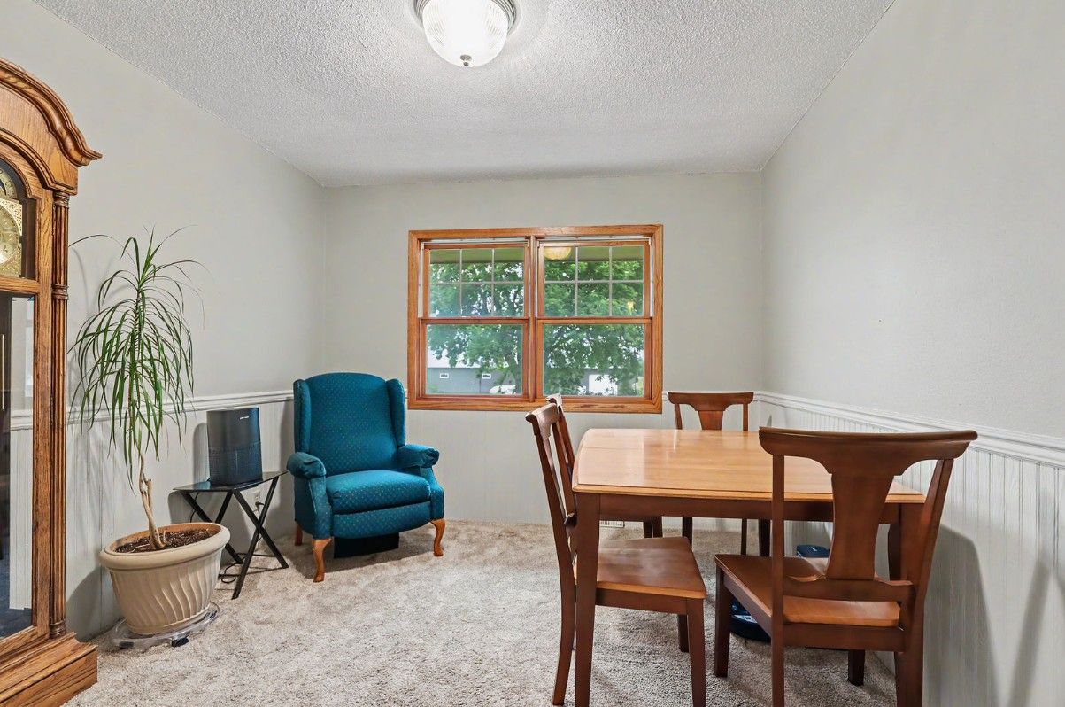 Dining room with wooden table and chairs, teal recliner, and large window in a bright carpeted room
