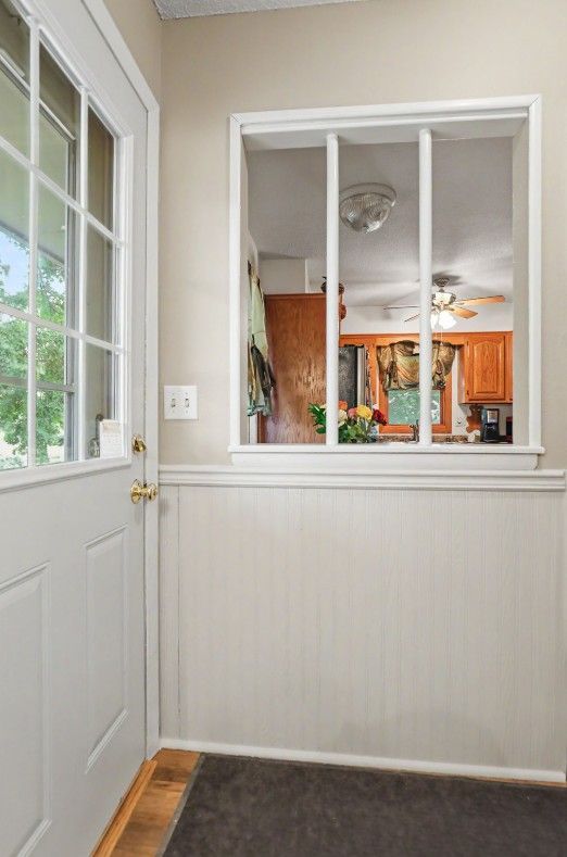 Bright white entryway with a glass door, window opening to a dining room, and gray carpet.