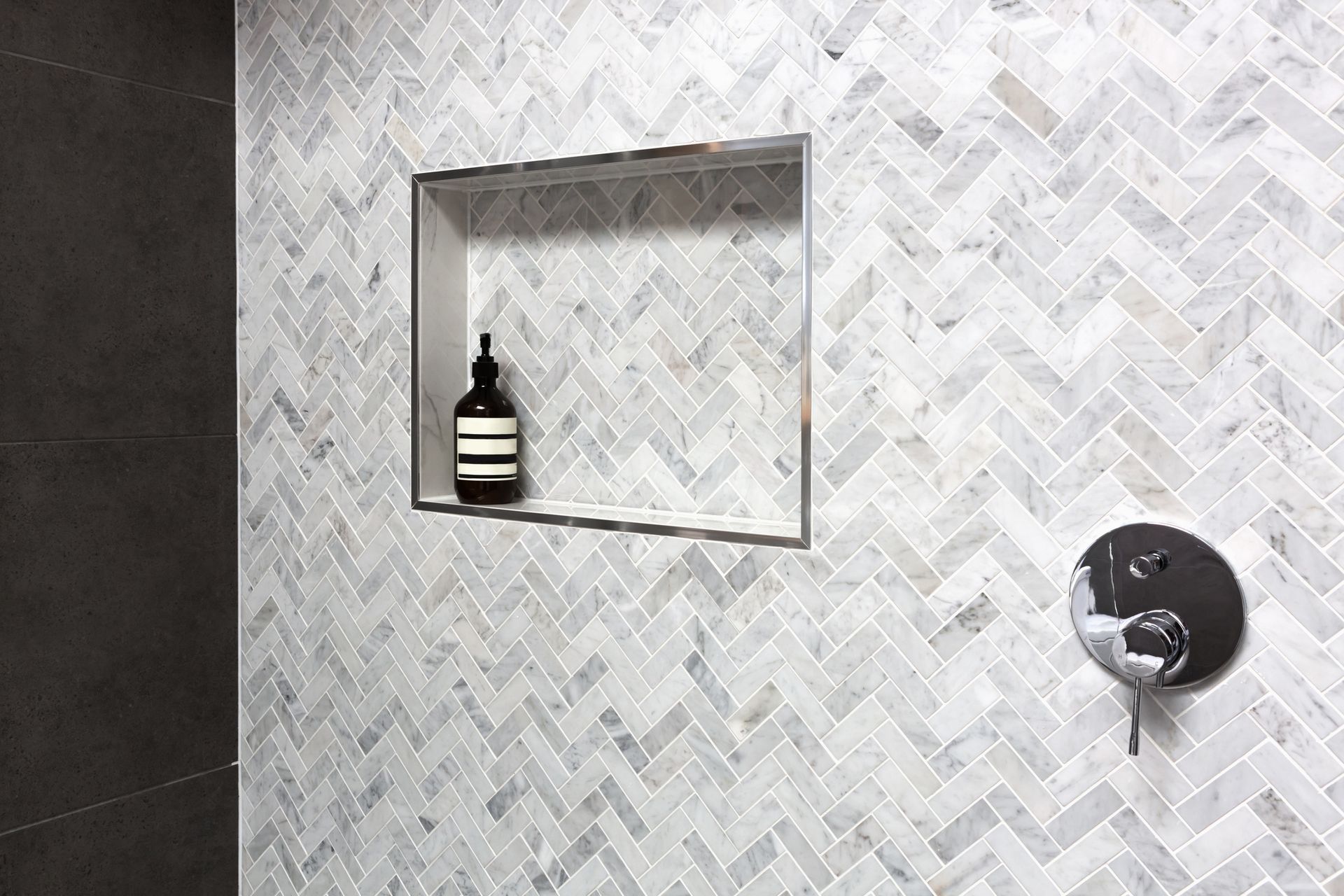 Modern tiled bathroom wall with recessed shelf, bottle, and chrome shower fixture