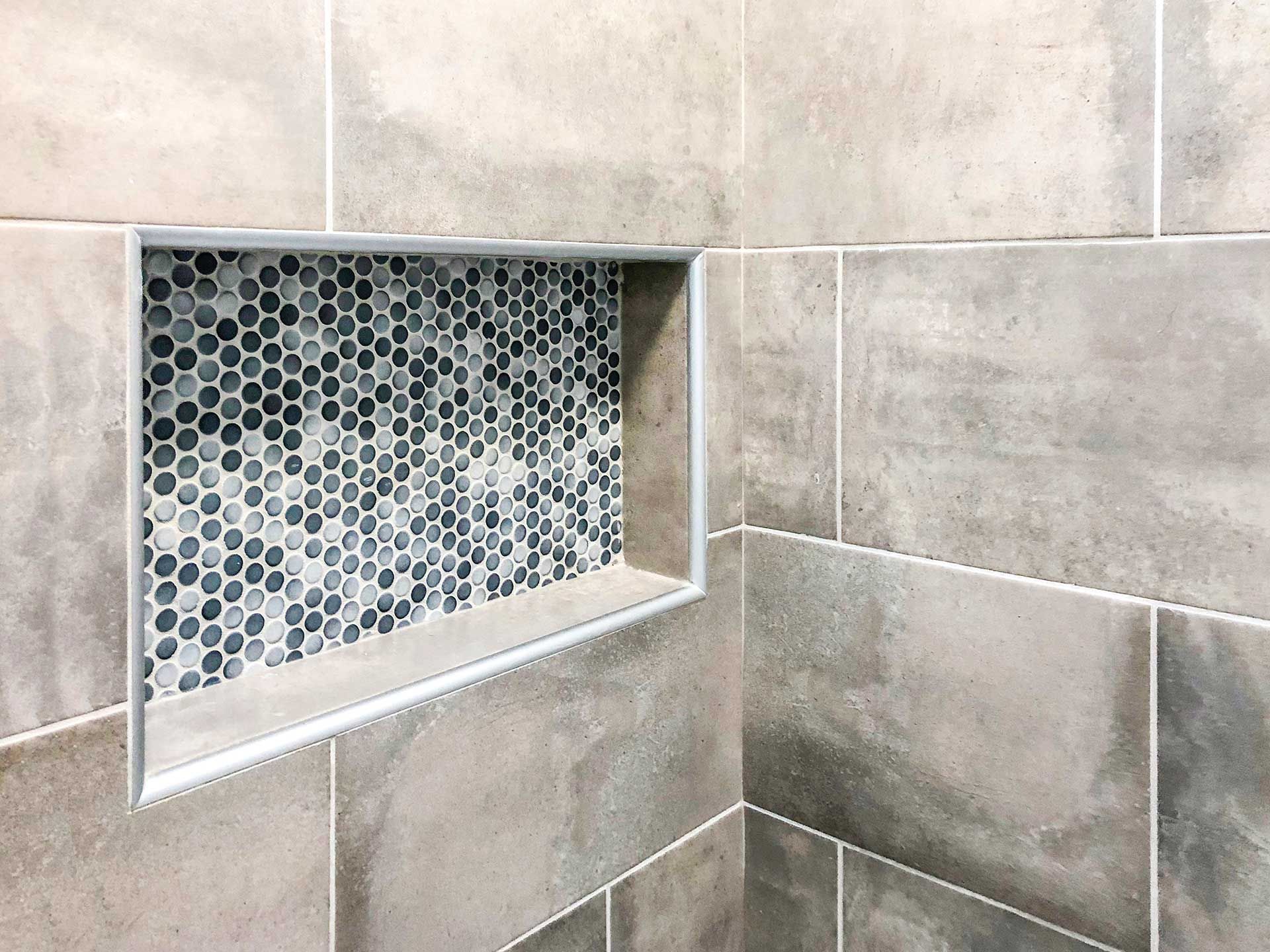 Small recessed wall niche lined with blue-gray mosaic tile in a beige tiled shower wall