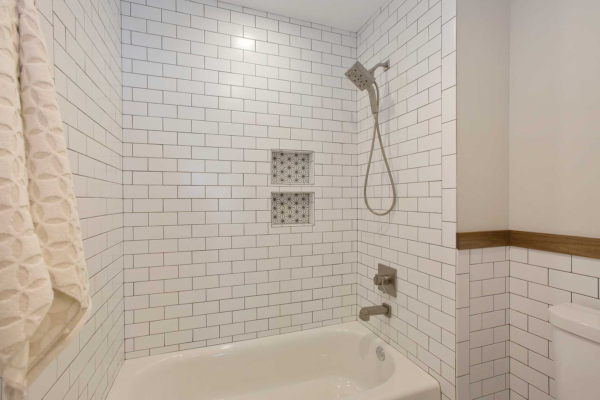 White tiled bathroom shower and bathtub with handheld showerhead and beige towel rack