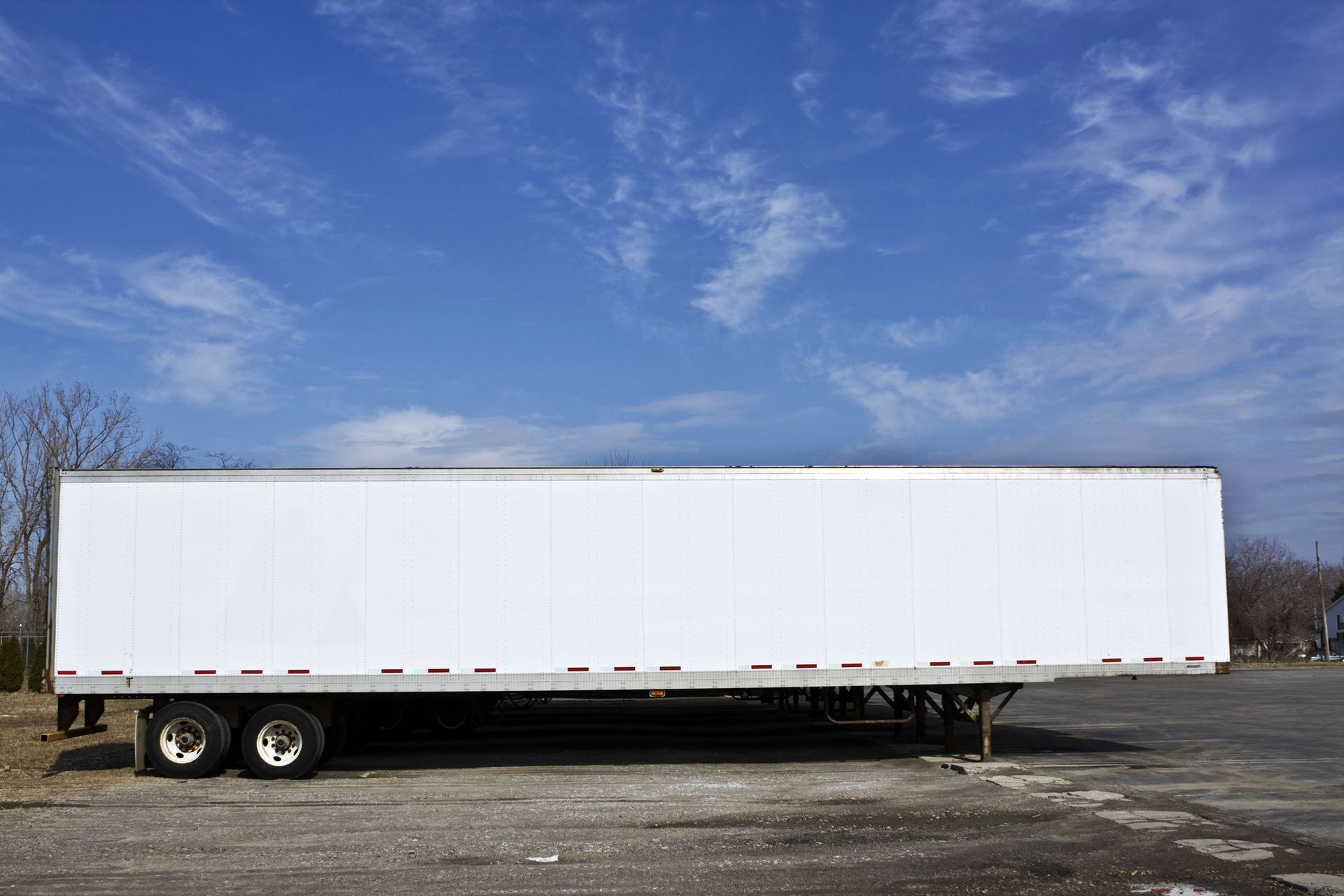 White semi-trailer parked on asphalt against a blue sky with scattered clouds.