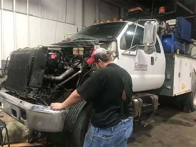 Mechanic inspecting a white service truck with the hood open in a garage.