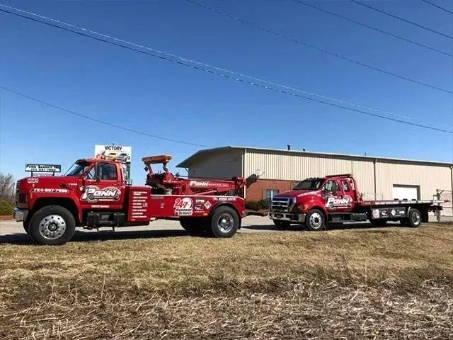 Two red tow trucks parked outdoors on a sunny day.