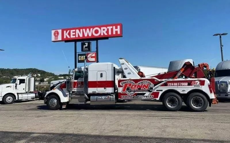 Tow truck with red and white detailing parked under a Kenworth sign.
