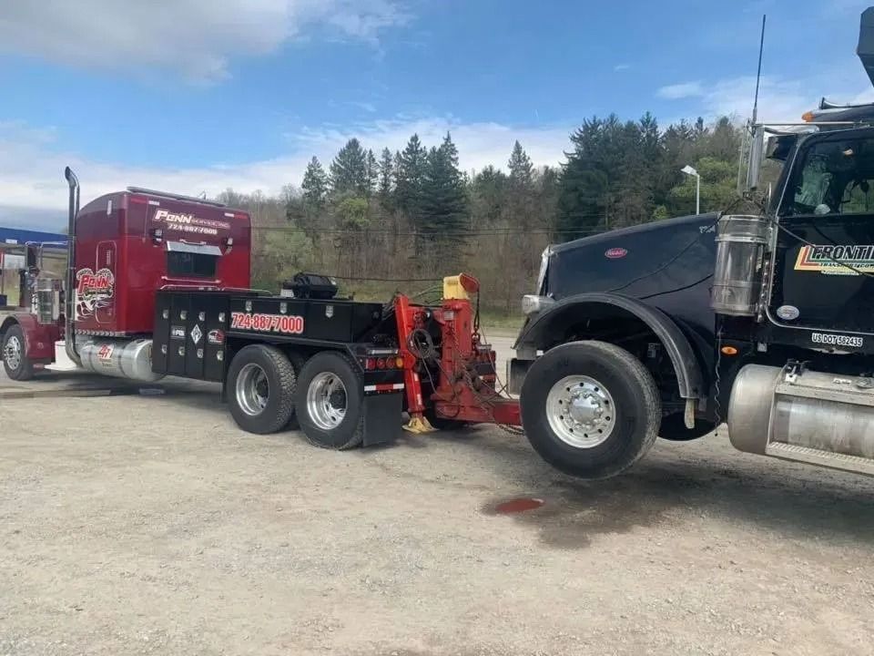 A burgundy tow truck towing a black semi-truck on a sunny day.