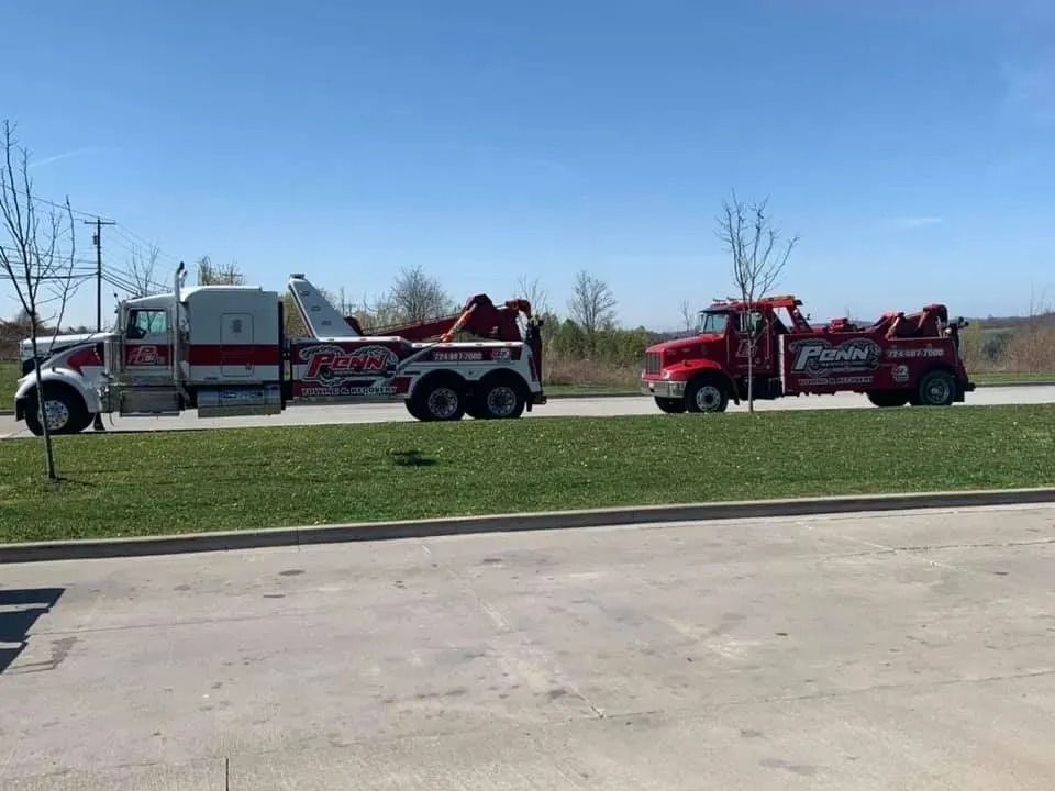 Two tow trucks: a large white/red one towing a smaller red truck on a sunny day.